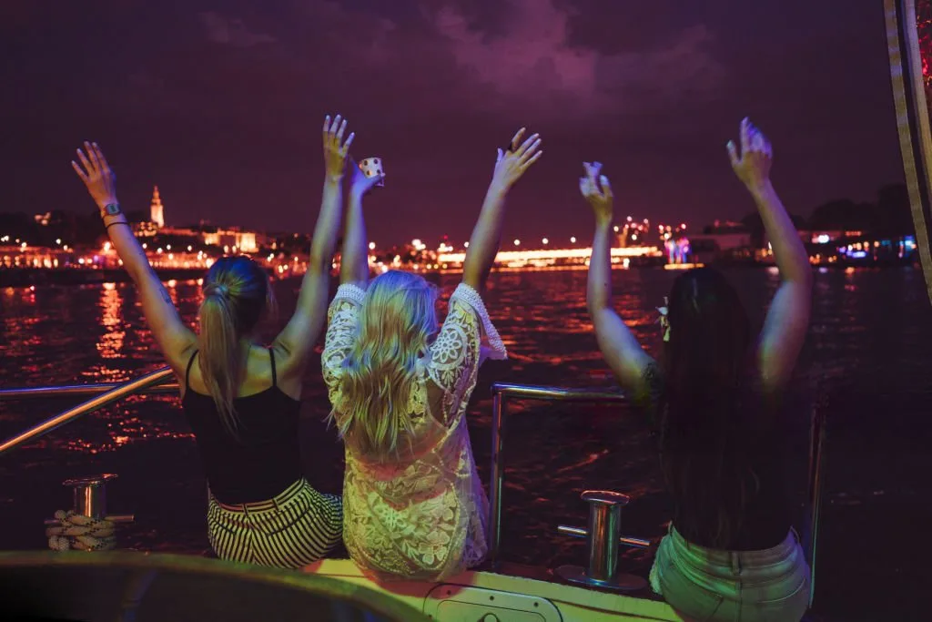Ladies enjoying on the boat at night Three women are sitting with hands raised on the deck of the boat at night. Party - elite pearl charter